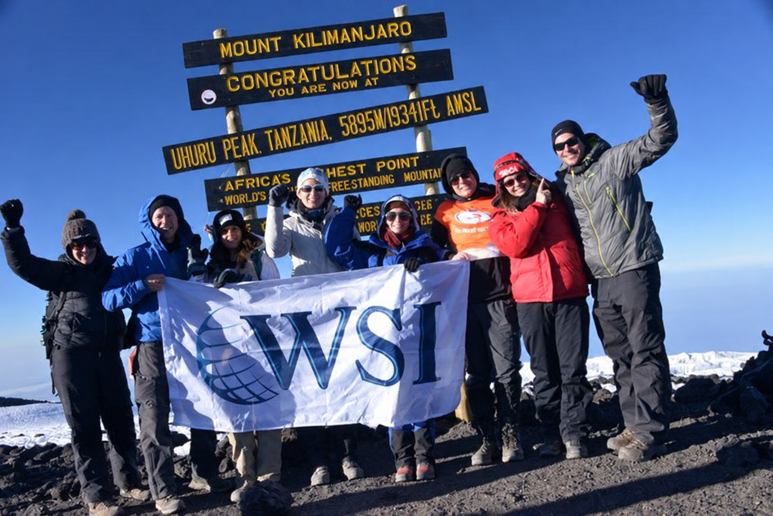 The WSI team holding the WSI flag at the Uhuru Peak summit sign on Mount Kilimanjaro