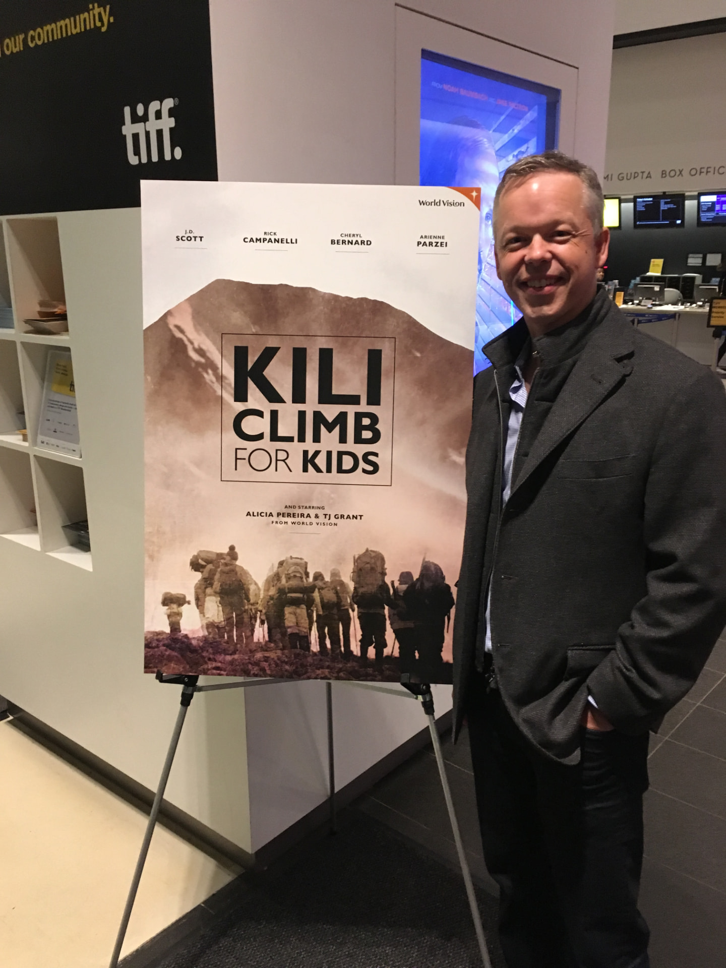 Dan Monaghan beside the Kili Climb for Kids film poster at TIFF Bell Lightbox