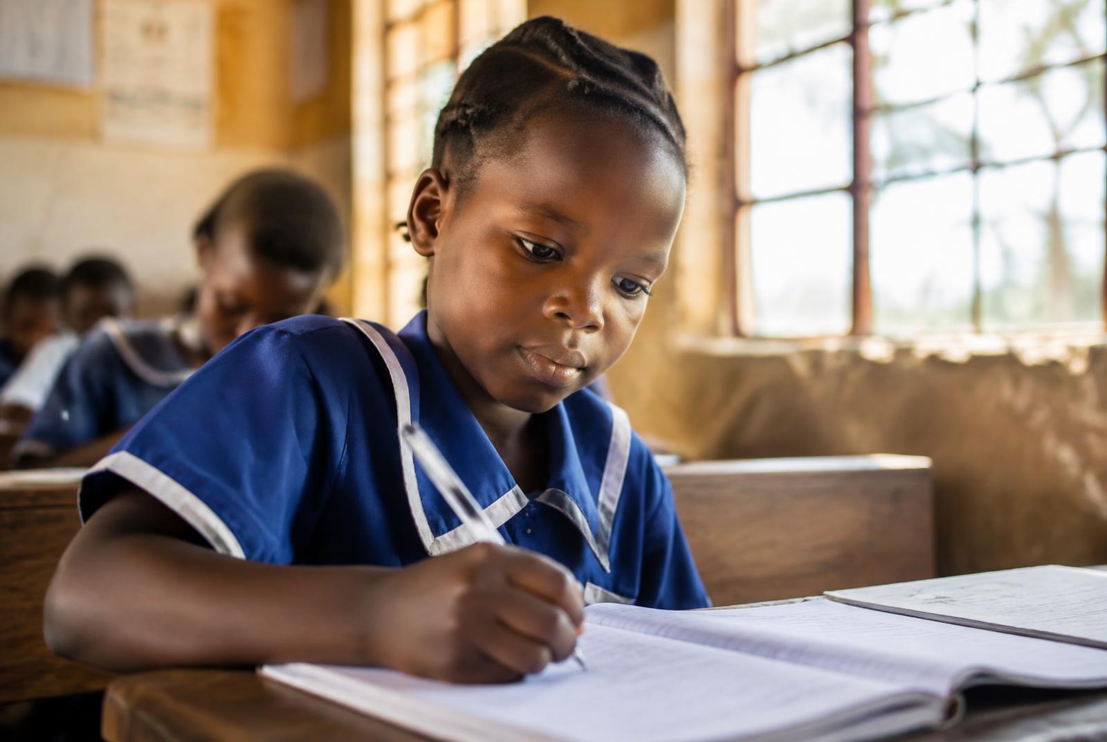 A girl writing in her notebook in a sunlit classroom